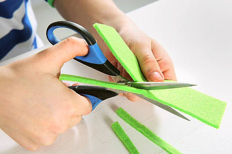 Lassen Sie Ihr Kind den grünen Filz in schmale Streifen schneiden.
