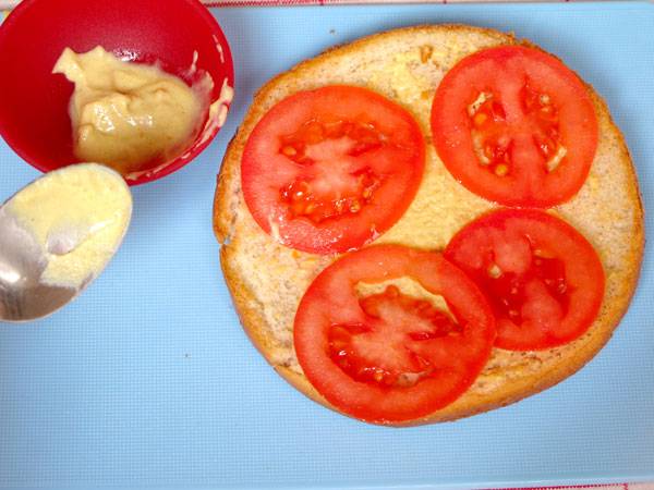 Belegen Sie die Burgersemmeln mit Tomaten